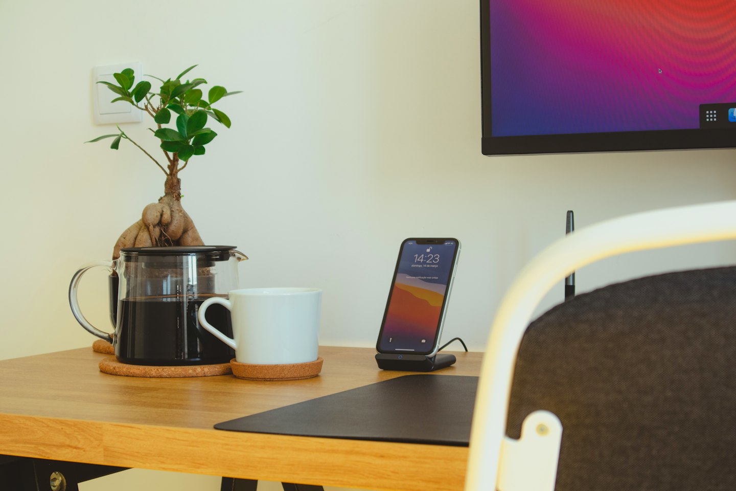 Ein aufgeräumter hölzerner Schreibtisch mit einer Kaffeekanne und einem Bonsai.
