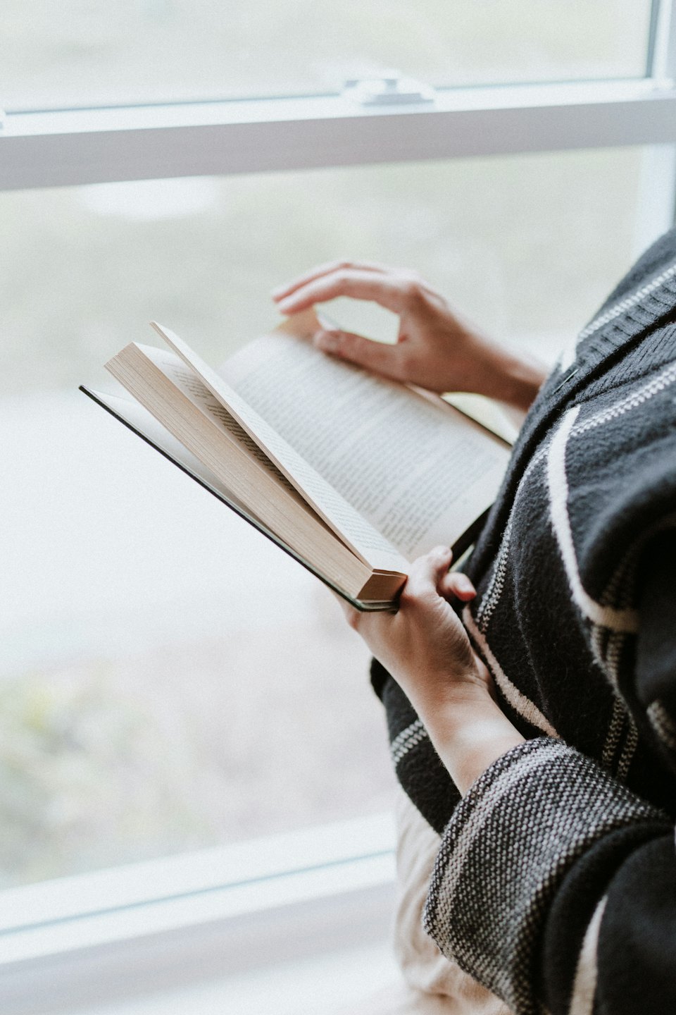 Eine Person liest ein offenes Buch in der Nähe eines Fensters.